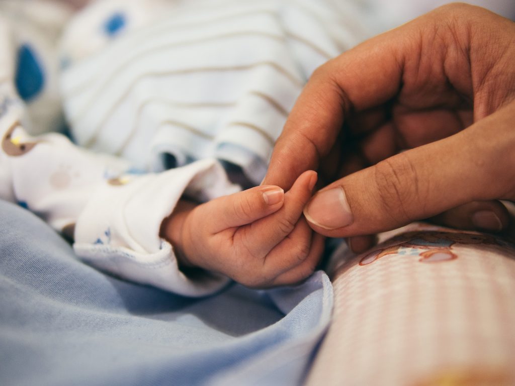 Large hand holding the hand of a newborn baby