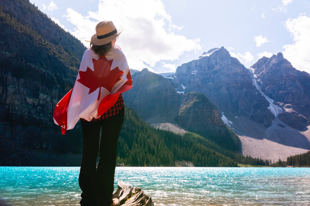 Woman with a Canadian flag wrapped around her while standing in front of lake